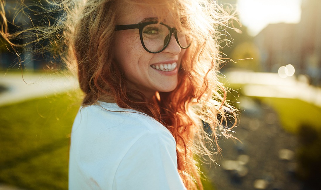 A smiling red-haired woman standing outside during the sunset