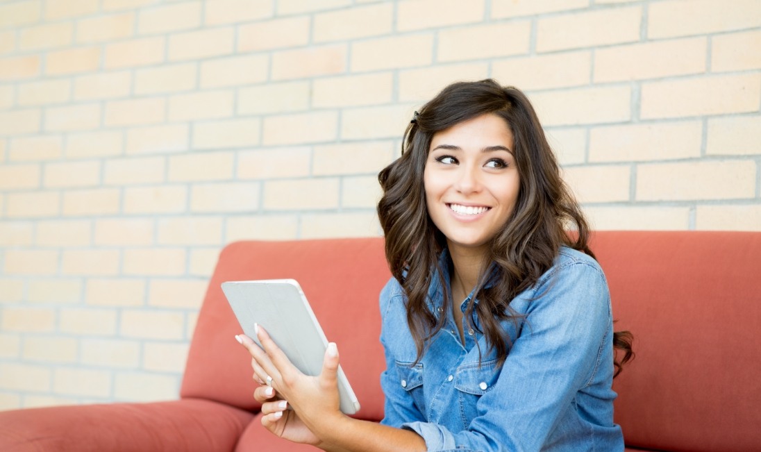 Smiling woman in denim shirt sitting on couch and holding tablet