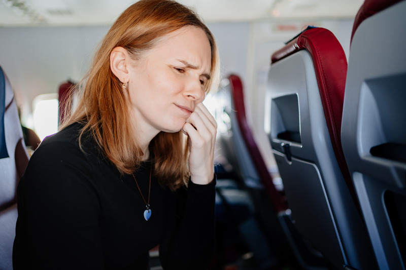 Patient on plane holding their cheek due to dental emergencies